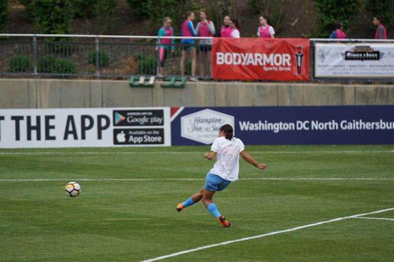 Sam Kerr practicing goal kicking. A small group of people watch on. 