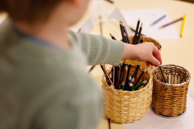 A young boy reaching for a pencil at childcare.