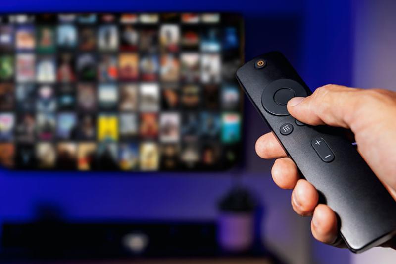 a person holds a television remote, pointing to a TV screen with streaming apps, that are blurred