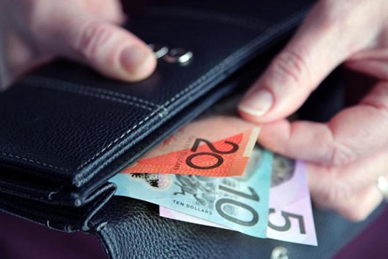 A hand pulling a $20, $10 and $5 note out of a wallet.