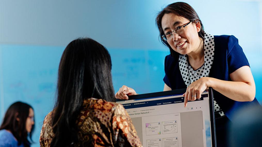 Teacher leaning over computer screen helping a student.