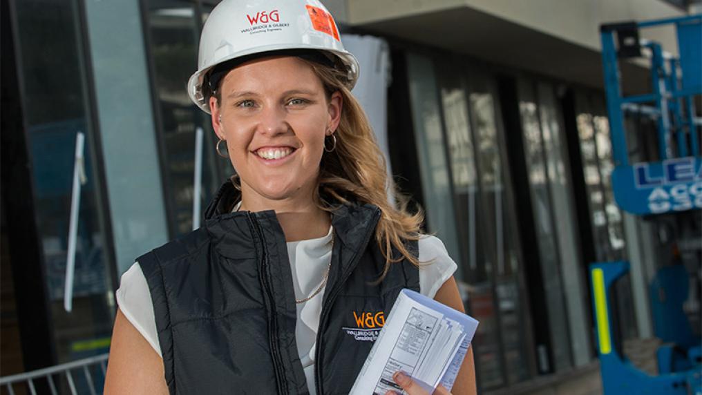 smiling female graduate, posing at a work site in vest and hard hat