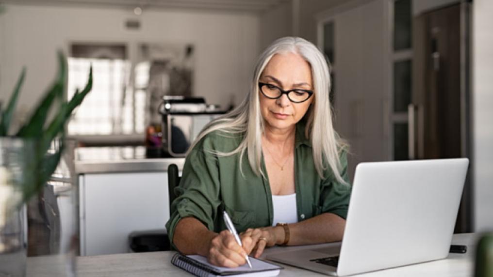 A person sitting in front of a laptop writes notes down on a pad of paper.