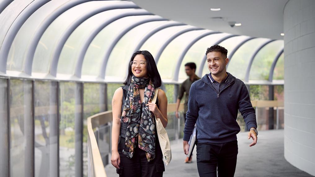 Two students walk down a light filled hallway.